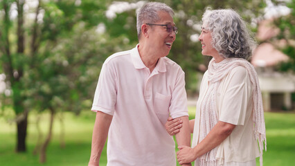 Happy Asian elderly couple enjoying retirement lifestyle walking arm in arm together in a peaceful green park outdoors