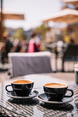 Two cups of coffee on a table in an outdoor cafe under bright sunlight