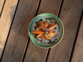 Colorful roasted vegetables artistically arranged in green ceramic bowl with herb garnish on wooden table surface