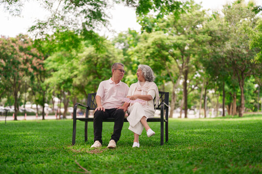 Older Asian couple happy park bench enjoy retirement leisure talking smiling sunny day