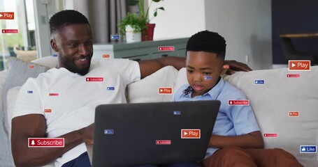 Father-son opening laptop on sofa showing floating play subscribe like icons exploring technology - Powered by Adobe