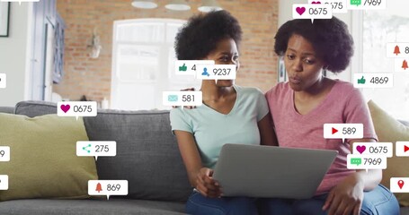 mother and daughter clicking laptop generating social media notifications floating around gray sofa - Powered by Adobe