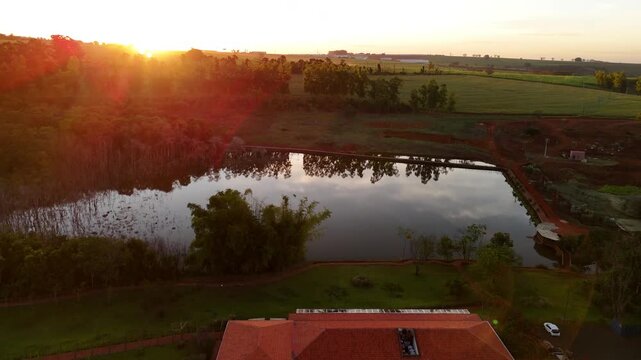 Vin&iacute;cola no Brasil vista por drone ao p&ocirc;r do sol, com lago ao lado, natureza exuberante,  vinhedo iluminados pela luz dourada. Beleza rural, clima tranquilo e paisagem cinematogr&aacute;fica