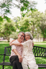 Naklejka premium Happy Asian older couple hugging on park bench enjoy retirement life outdoors senior lifestyle