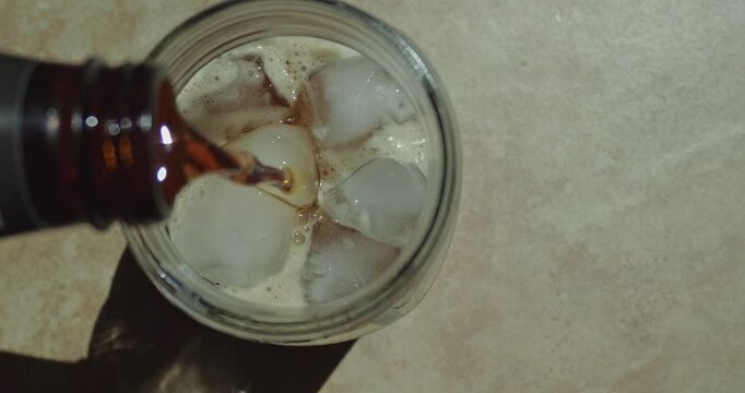 Look down at soda pouring into a cup with ice in slow motion 