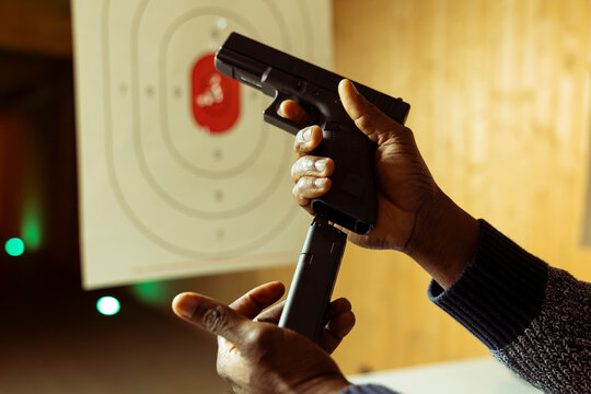 Close up of hands loading handgun magazine at indoor shooting range with paper target in blurry background. Person doing firearm training, learning how to responsibly reload pistol
