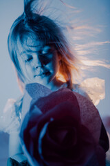 Young girl holds a rose in artistic lighting with flowing hair and a thoughtful expression