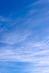 A vibrant blue sky featuring thin and sparse white cirrus clouds, spreading subtly, creating an atmosphere of lightness and tranquility.