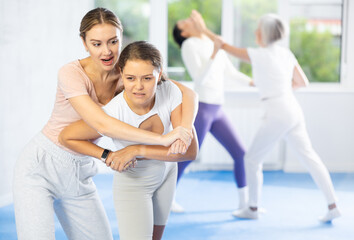 Emotional young woman trying to escape from back grip and delivering elbow strike to midsection to female opponent during mock bout in self-defense training..