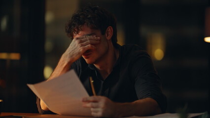 Fatigued manager feeling burnout reading documents at night office closeup.