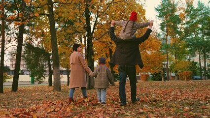 Happy children play, walk holding hands with mom, dad, autumn park with yellow leaves. Kid on dads shoulders, mom son play together, holding hands in autumn outdoor. Family walk weekend dad child mom