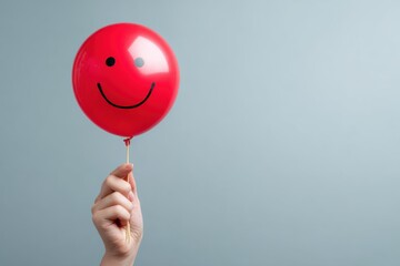 Hand holding smiling face red balloon, isolated background