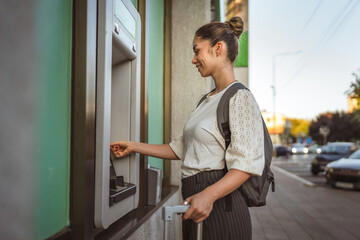 woman with baggage using credit card and withdrawing cash at the ATM