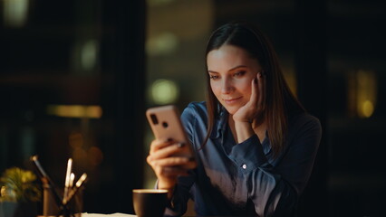 Relaxed businesswoman watching mobile phone taking break in dark office closeup.
