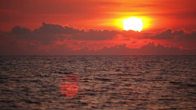 Large bright sun on red sky going down under the sea level at horizon on sunset, fast motion