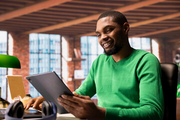 Happy remote employee watching comical videos on social media using tablet. Joyous person using...