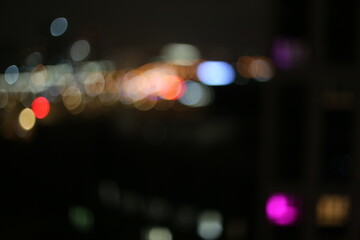 Defocused city lights at night with colorful bokeh effect. Blurry view of urban buildings and neon...