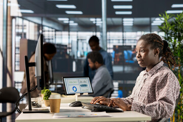 African american female professional works at desk in a corporation, working on financial planning and business strategy. Analyst focuses on company growth and effective resource allocation.