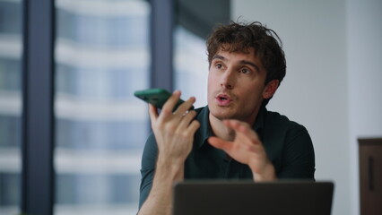 Freelancer dictating voice message at smartphone sitting agency office closeup.