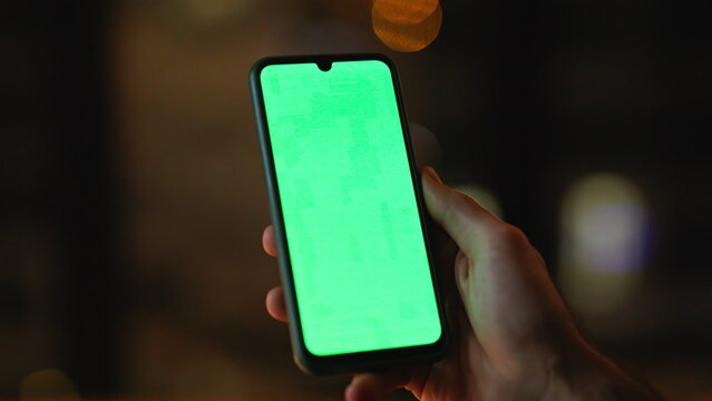 Guy hand holding green screen smartphone at night apartment closeup. Unknown man