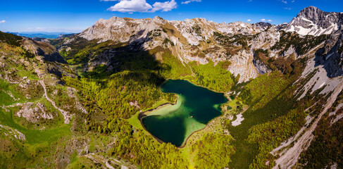 Aerial panoramic view of Trnovačko Lake, surrounded by lush green forest and dramatic mountain peaks in the heart of the Balkans, Montenegro. Summer landscape from drone.