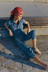lifestyle woman in modern boho-western denim street style sits relaxed on a concrete surface...