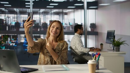 Cheerful proud CEO smiling at her photographs on smartphone, having fun on her work break at the...