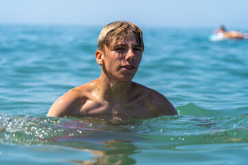 Close-up of a young male with wet blond hair in sparkling blue ocean water on a bright summer day,...