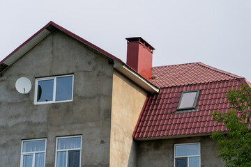 Residential Building Facade with Modern Red Metal Roof, Chimney, Windows, and Satellite Receiver Installation.