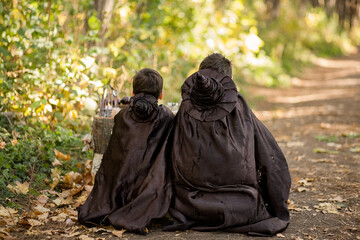 Two teenagers dressed as wizards sit in a forest, embracing the mystical atmosphere. View from the...