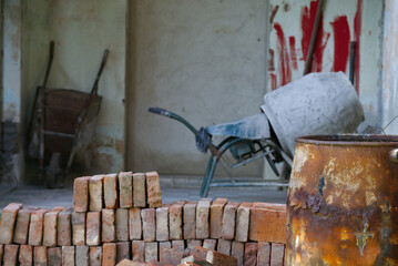 Bricks, cement mixer, wheelbarrow and rusty barrel in abandoned construction site