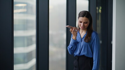 Businesswoman recording phone audio notification standing at window closeup.