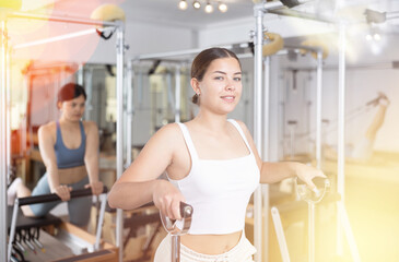 Sporty young girl practicing pilates in fitness studio, doing stretching exercises on wunda chair..