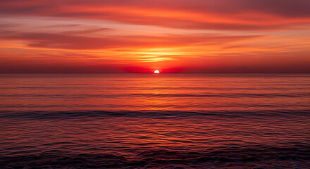 Obraz premium Crimson Sunset on the Horizon: The sun dips below the horizon, casting a vibrant crimson glow across the ocean. The sky bursts with fiery hues, while the calm water reflects the colorful sunset.