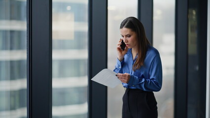 Calling woman worried documents mistake standing by office window closeup.