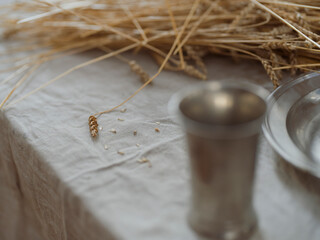 Wheat stalks with pewter vessels on white tablecloth in traditional communion setting with natural light