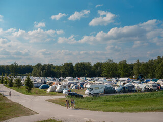 Large camping site with numerous tents caravans and blue sky on sunny summer day