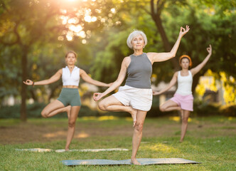 Elderly woman doing yoga on mat in group of women in park