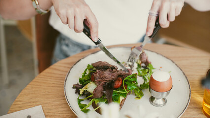 Female hands holding a knife and fork in front of a plate with salad and meat. Healthy eating. Healthy Lifestyle.  Close-Up.  Soft focus.