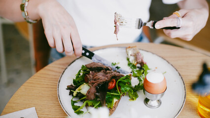 Female hands holding a knife and fork in front of a plate with salad and meat. Healthy eating. Healthy Lifestyle.  Close-Up.  Soft focus.