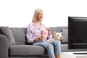 Woman with a dog eating popcorn, watching tv and sitting on a sofa