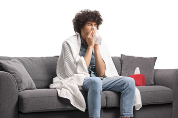Guy wrapped in blanket sitting on a sofa and blowing nose