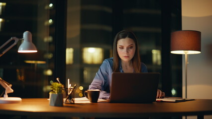 Shocked businesswoman reacting failure looking laptop at night company office.