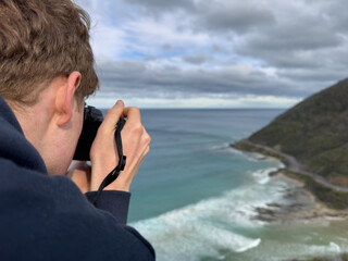 Teenage boy photographing scenic Great Ocean Road coast with mountain and ocean