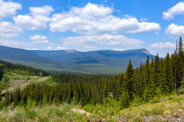 Scenic landscape among mountains, forests and meadows in summertime, blue cloudy sky above, sunny...