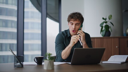 Irritated businessman yelling mobile phone sitting office desk looking laptop.