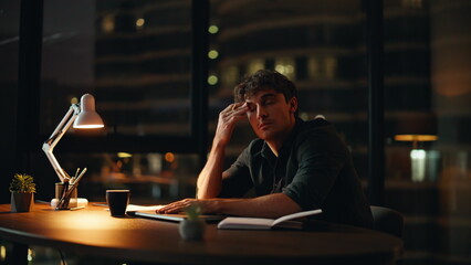Fatigued employee sitting dark workplace with closed laptop. Overworked manager