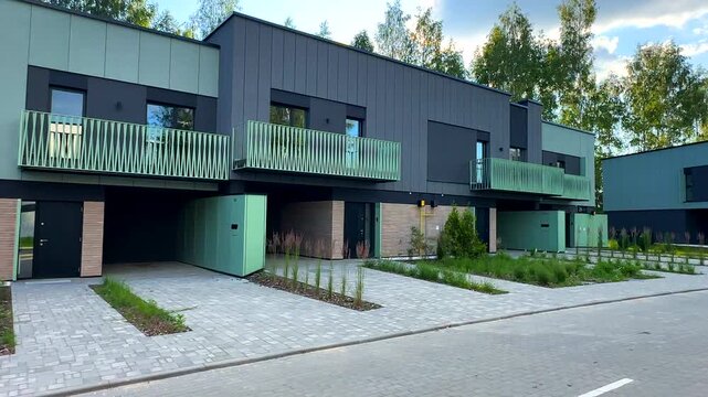 Modern townhouse with green facade building exterior. Modern two-story house with garage, balcony. Ornamental thuja, shrub juniper in yard. Front yard building exterior of townhouse. Modern townhome.