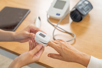 Asian woman doctor measuring blood oxygen levels to senior female patient at nursing home....
