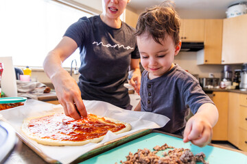 Mother and Toddler Boy Collaborating to Make Homemade Pizza in the Kitchen